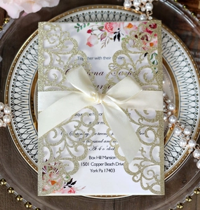 Macro view of laser-cut glitter gold wedding invitation with ribbon on a plate