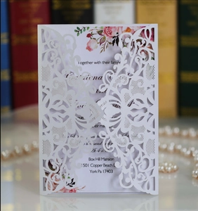 Macro detail of laser-cut pearl white wedding invitation with floral watercolor inner page