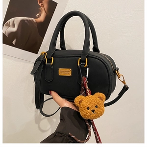 Detail of black matte leather boston bag with golden plaque and yellow teddy bear charm