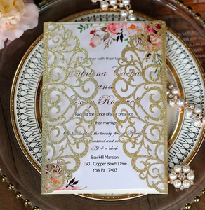Detail of laser cut gold glitter wedding invitation with floral card on elegant glass plate