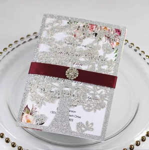 Close-up of laser-cut silver glitter wedding invitation with burgundy ribbon and rhinestone