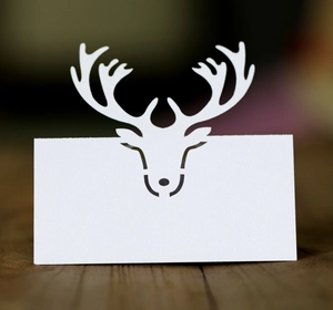 Detail of white laser-cut reindeer place card on dark wood table for weddings