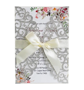 Detail of laser-cut glitter wedding invitation with ivory silk ribbon and floral insert