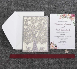 Detail of silver glitter laser cut tree invitation with white floral card and burgundy ribbon