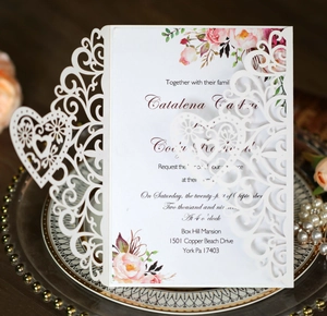 Detail of laser-cut lace wedding invitation with floral interior on vintage tray