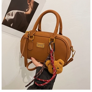 Detailed side view of a brown leather bowling bag with gold logo and plush bear charm