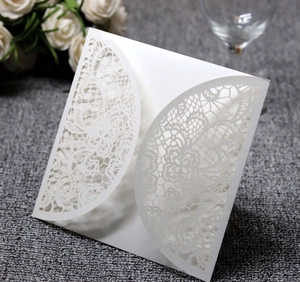 Detail of laser-cut white lace invitation card with pearl finish on dark textile surface