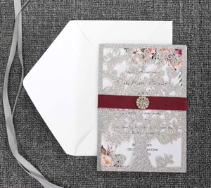 Detail of silver laser-cut invitation with red silk ribbon and crystal brooch decoration
