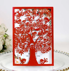 Detail of red laser-cut invitation card with tree and bird patterns on a ceramic tray