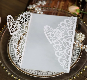 Detail of laser-cut heart and floral patterns on elegant white wedding invitation card