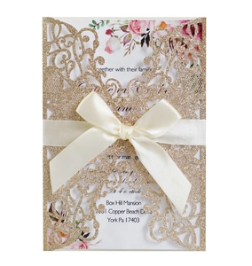 Close-up of laser-cut gold glitter invitation with elegant ribbon and floral inner card