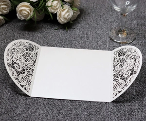 Detail of laser-cut lace pattern on white wedding invitation cards with floral motifs