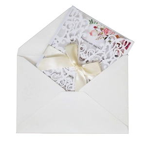 Detail of laser-cut white wedding invitation with elegant floral patterns and satin bow