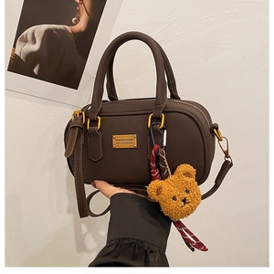 Detail of deep brown Boston handbag featuring gold metal plate and plush bear charm