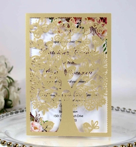 Detail of laser-cut invitation featuring golden tree and bird motifs on a white plate