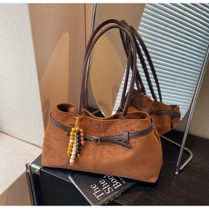 Close-up of brown suede tote bag with wooden bead pendant on dark wooden surface