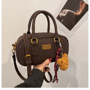 Detailed close-up of dark brown bowling bag with gold hardware and plush bear charm