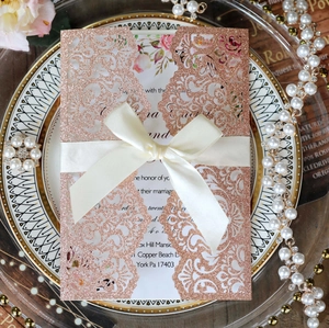 Detail of rose gold glitter laser-cut wedding invitation with cream satin ribbon bow