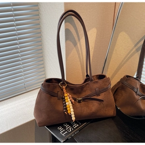 Close-up of deep brown suede tote bag with decorative metal buckle and beaded pendant