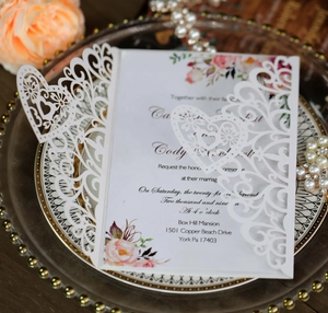 Detailed view of laser-cut wedding invitation with floral insert on glass plate