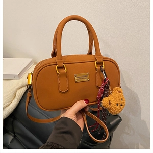 Close-up of brown leather bowling bag featuring a plush bear charm and gold metal plate
