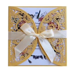 Macro detail of laser-cut wedding invitation with gold lace casing and white satin bow