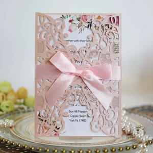 Detail of pink laser-cut wedding invitation with floral patterns and a satin bow