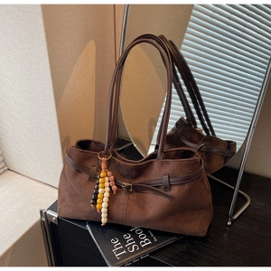 Close-up of vintage brown suede tote bag with decorative buckle and beaded tassel charm