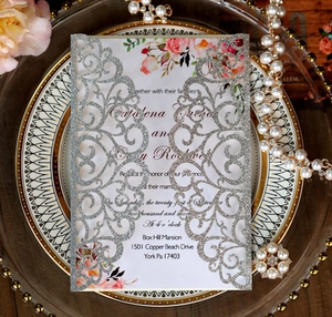 Detail of silver laser-cut wedding invitation with floral insert on a display tray