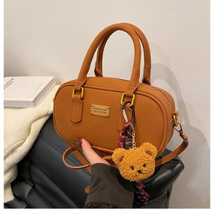 Close-up of caramel brown leather bowling bag with cute plush bear charm on a sofa