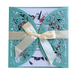 Detail of laser-cut turquoise lace wedding invitation with cream ribbon and floral insert