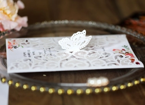 Detail of white laser-cut wedding invitation featuring butterfly lace and floral insert
