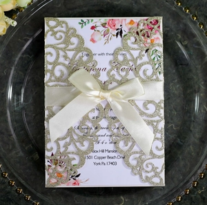 Detail of laser cut gold glitter wedding invitation with white satin bow and floral insert