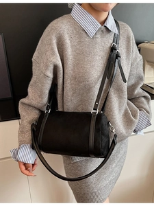 Minimalist black cylinder shoulder bag in matte finish with adjustable strap worn by model