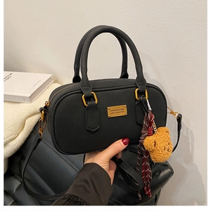 Detail view of black boston bag with gold hardware, bear charm and ribbon scarf accent