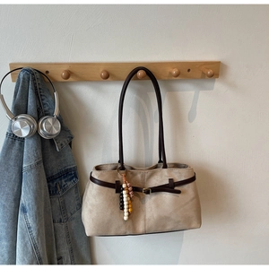 Detail of vintage beige suede tote bag with beaded charm hanging on a wooden hook