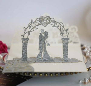 Détail d'un faire-part de mariage 3D découpé au laser avec paillettes argentées et couple
