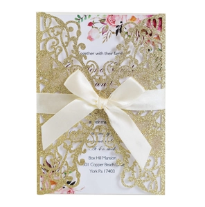 Detailed laser-cut gold glitter wedding invitation with elegant satin bow and floral insert