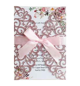 Detail of rose gold laser cut wedding invitation with pink satin bow and floral inner card