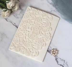 Détail d'une invitation ajourée blanc crème sur marbre avec des roses et décor vintage