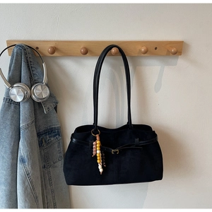 Detail of black suede tote bag with metal buckle and colorful ethnic beaded charm accessory
