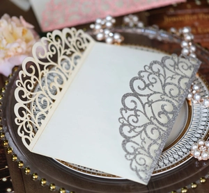 Intricate laser-cut floral scrollwork on a silver glitter and cream wedding invitation cover