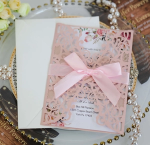 Detail of pink laser-cut wedding invitation with elegant satin bow and floral inner page