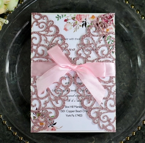 Close-up of laser cut glitter wedding invitation with pink satin ribbon and floral card