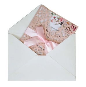 Detail of laser-cut wedding invitation with pink ribbon bow and floral inner card