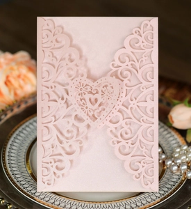 Detail of pink laser-cut heart invitation cover with elegant pearl finish on a gold-rimmed plate