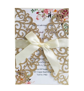Macro view of laser cut gold glitter floral wedding invitation with satin ribbon detail