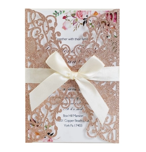 Detail of laser-cut glitter wedding invitation with cream satin bow and floral inner card
