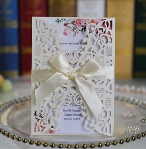 Detail of laser-cut wedding invitation with cream hollow shell and beige satin bow