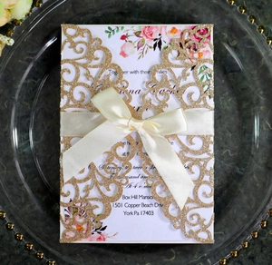 Detail of laser cut gold glitter wedding invitation with ribbon and floral insert card